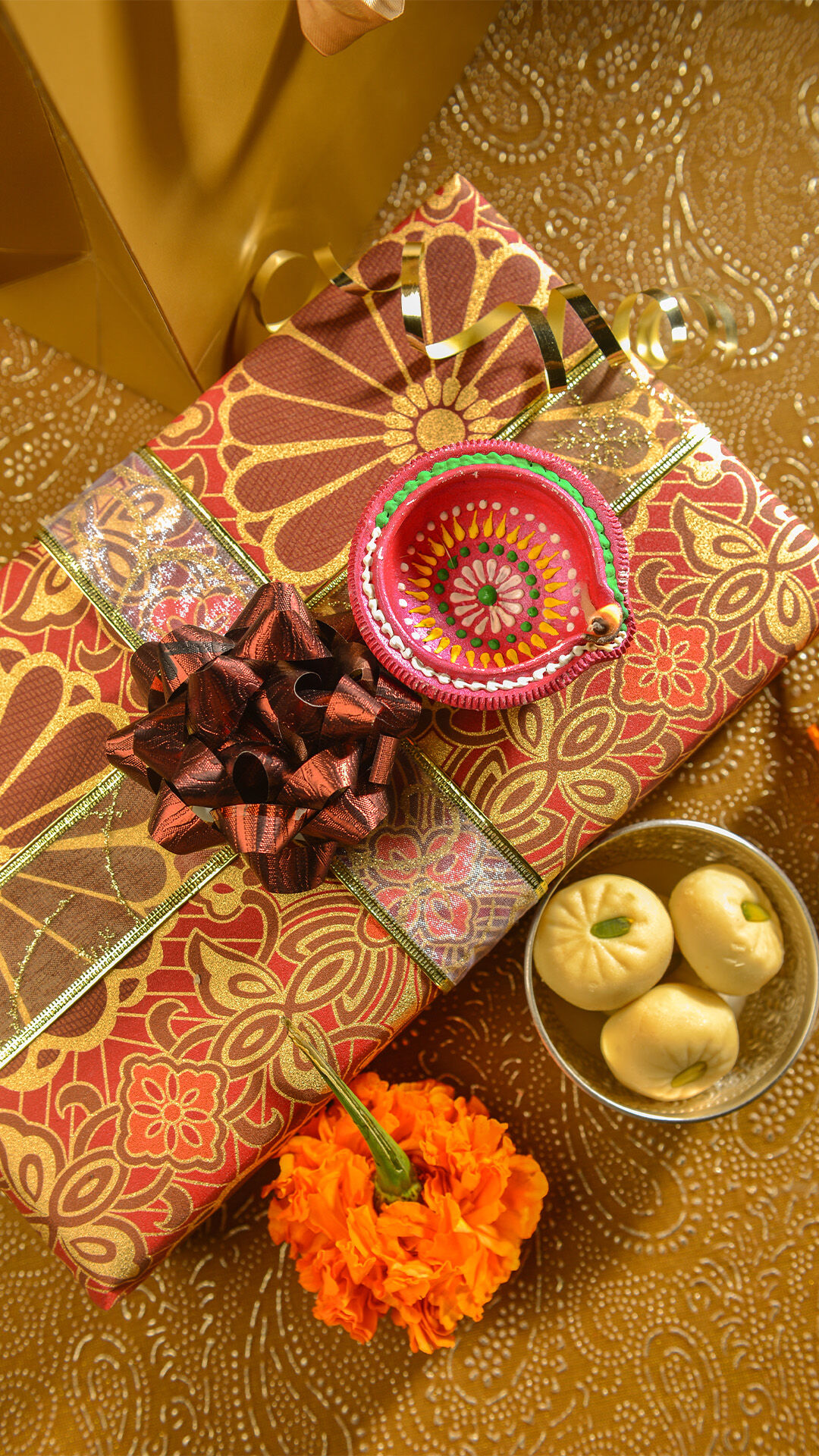 Handcrafted diya, traditional sweets, and saree in a decorative wedding gift package.